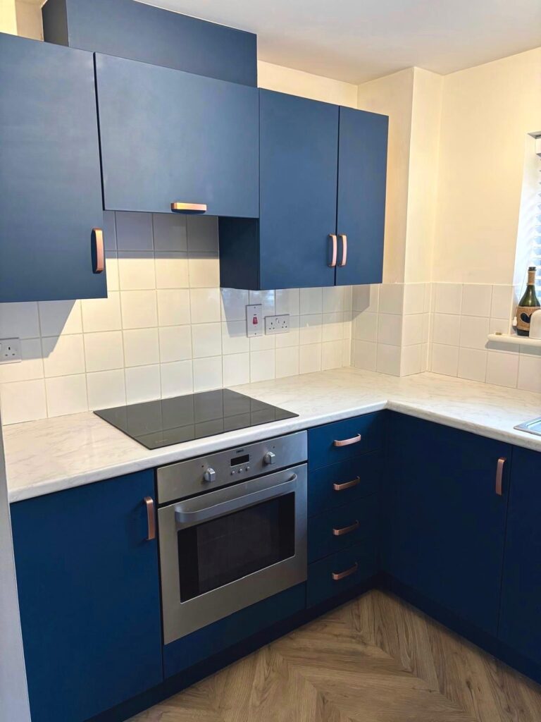Blue vinyl wrapped kitchen cabinets and white worktops beside the hob