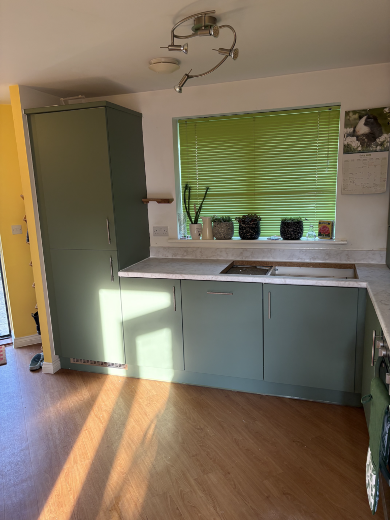 Green wrapped kitchen cupboards beside a window in Dereham