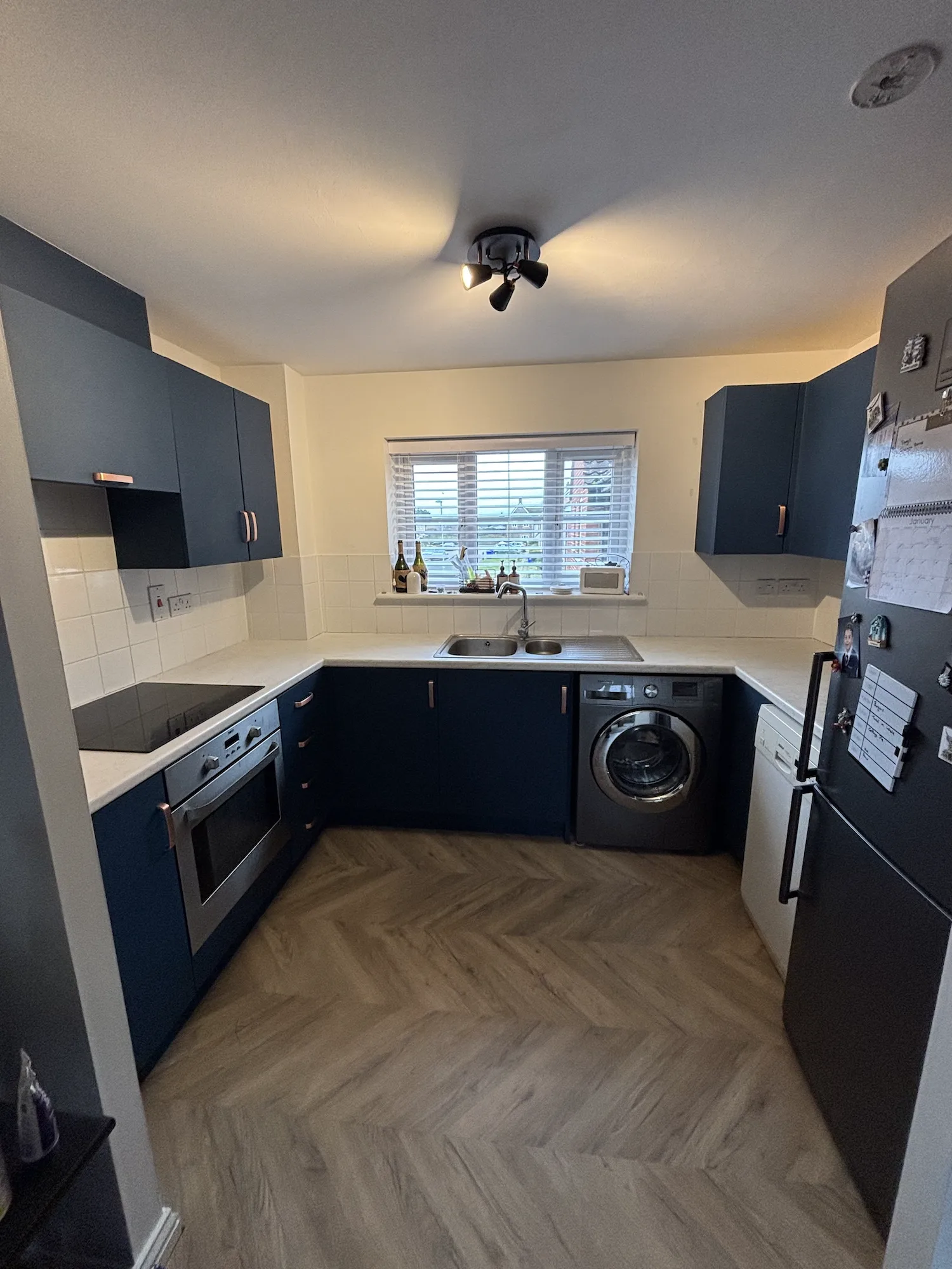 Completed matte navy kitchen wrap in Newmarket with white marble-effect worktops and brushed bronze handles