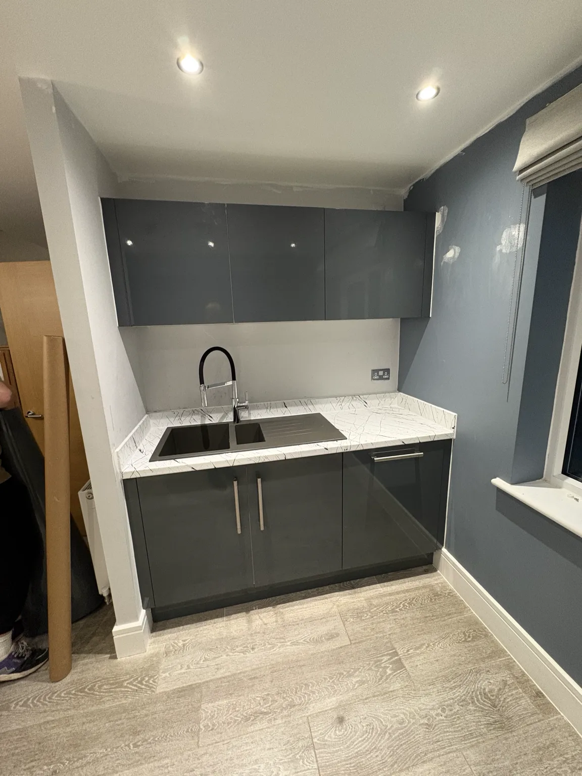 Swaffham kitchen with gloss grey wrapped cupboards and white marble-effect worktop around the sink